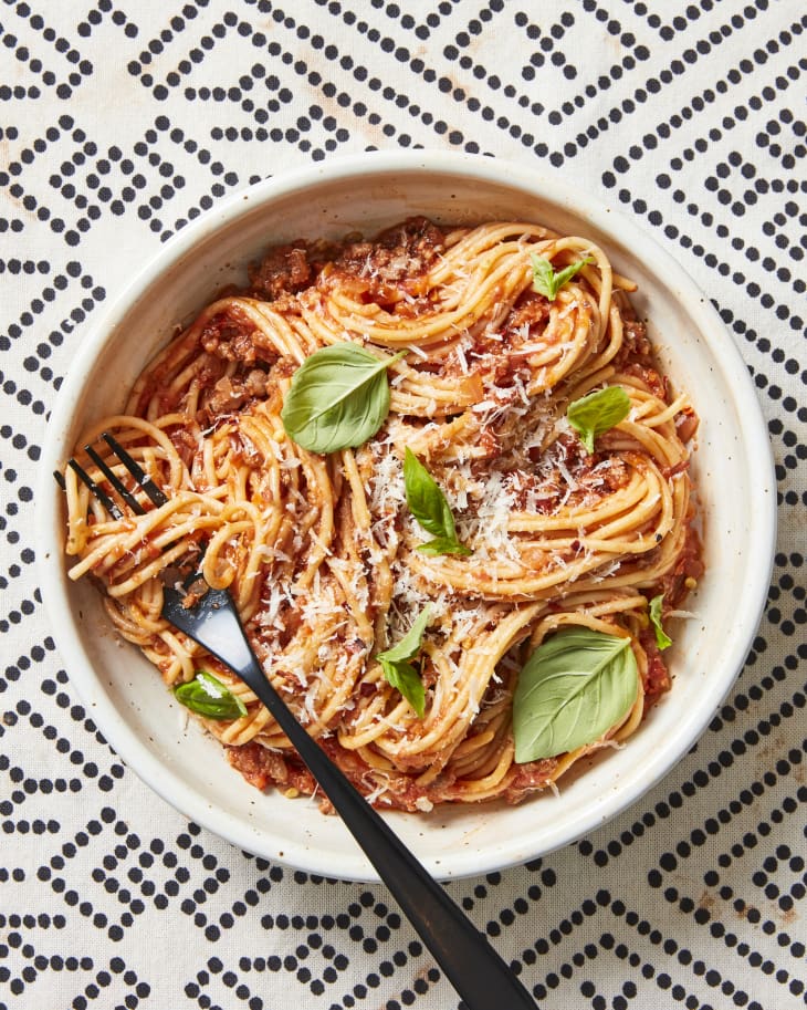 Spaghetti with meat sauce sprinkled with fresh grated parmesain, and basil in a bowl